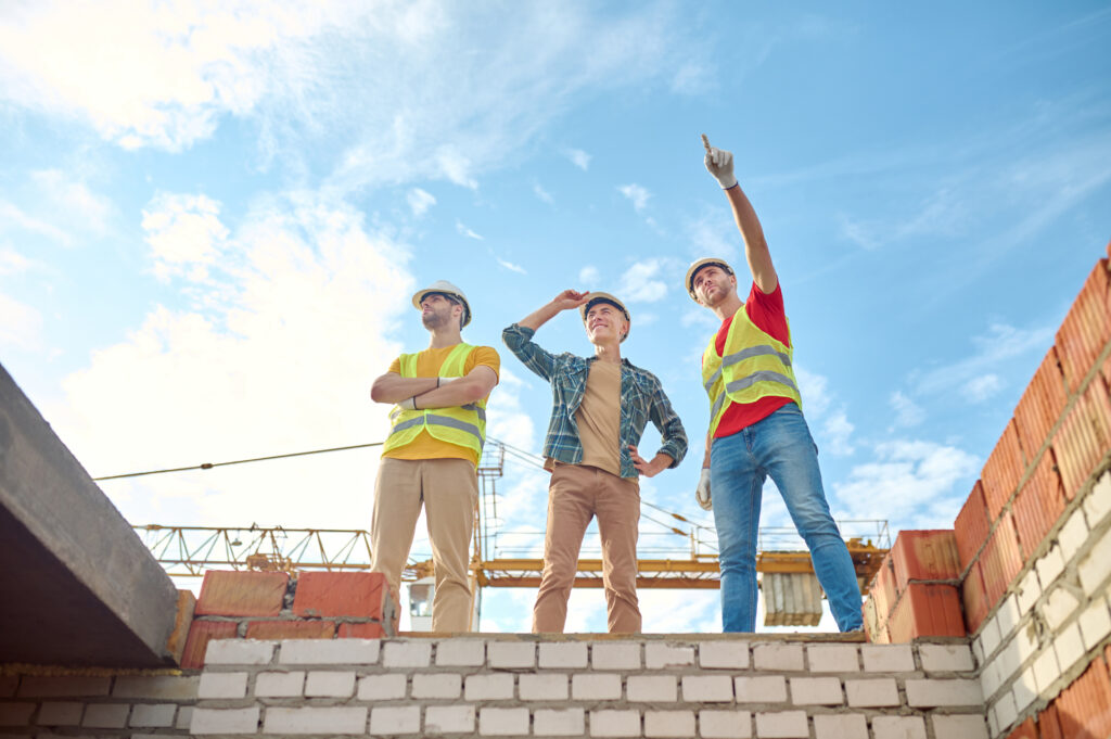 Men standing brick wall building construction roofing followup